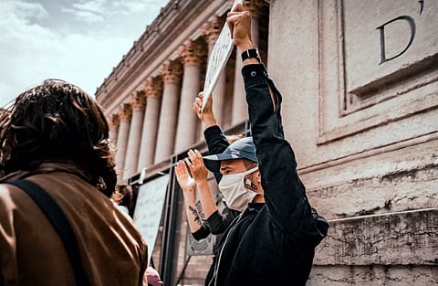 Masked protesters demonstrating in Lyon, France, with placards expressing social justice themes.
