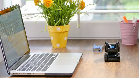 Stylish workspace featuring a laptop, toy robot, and vibrant flowers in natural light.
