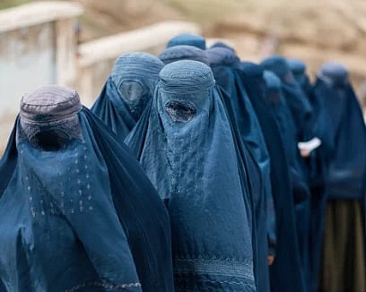 A group of women in blue burqas walk through a mountainous area in Afghanistan.
