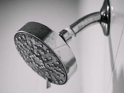 Black and white photo of a sleek, metal showerhead mounted on a bathroom wall.