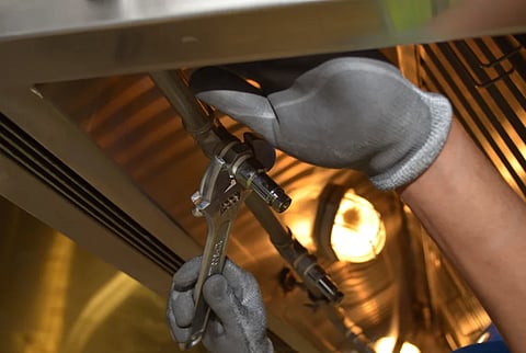A worker fixing pipes with tools in an industrial indoor environment.
