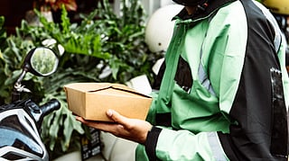 Food delivery rider with mask and helmet holding a package outdoors.