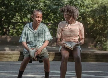 Two children sitting on a bench in a sunny park, engaged in reading books.
