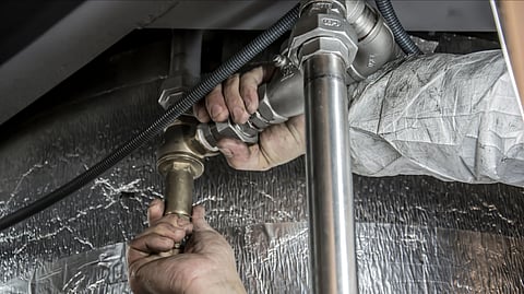 Close-up of a plumber's hands installing steel pipes indoors, showcasing skilled manual work.