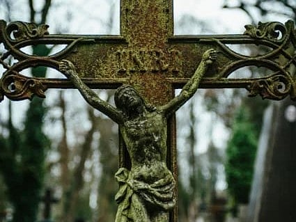 Vintage crucifix with Jesus in dense cemetery setting, hinting at timeless spirituality.
