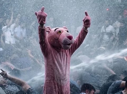 Image of a man in a pink panther costume during the French protest. he is surrounded by people on ground who are being aimed with water gun by the authorities 