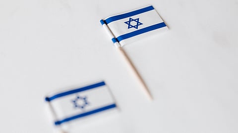 Close-up of two miniature Israeli flags on toothpicks with a white background.
