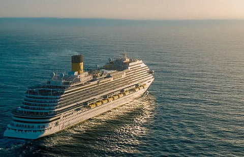 A breathtaking view of a cruise ship sailing across the ocean with the sun setting in the background.
