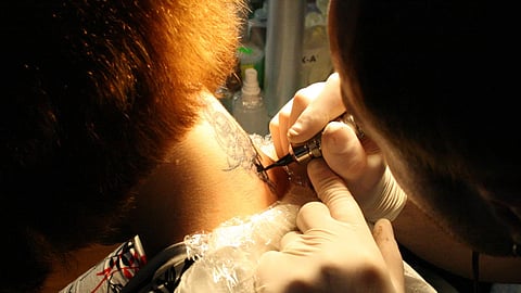 A tattoo artist painting their art on a customers neck