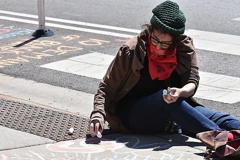 A woman creates chalk art on a Chicago street, highlighting activism and creativity.

