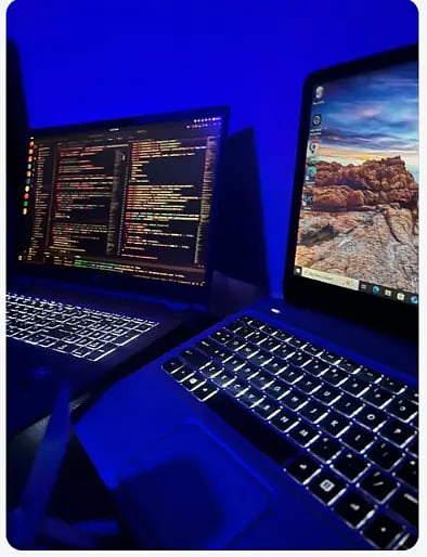  A pair of laptops displayed against a blue light backdrop, emphasizing their contemporary features and aesthetics.
