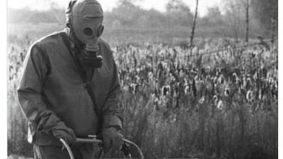 A man wearing a gas mask pushes a baby carriage down a street,