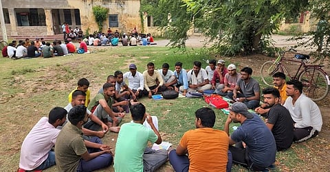 Men gather in a seated circle on a grassy courtyard for a focused discussion.