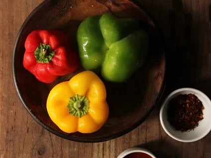 Top view of vibrant bell peppers with spices arranged on a wooden table.
