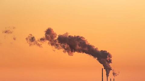 Smoke billowing from industrial chimneys against a vibrant orange sunset sky in Gdańsk, Poland.
