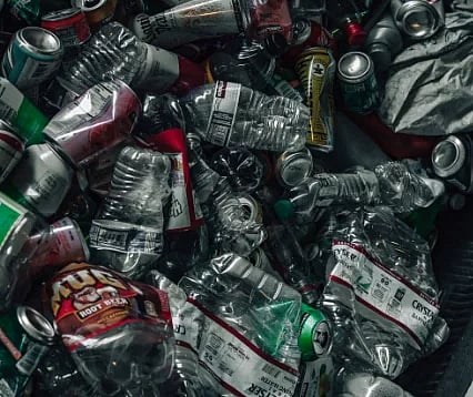 A vertical shot of a pile of recyclable plastic and metal containers in a recycling bin, emphasizing sustainability.
