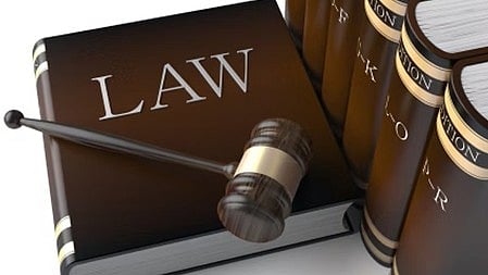 इस तस्वीर में एक कानून की किताब है और उसके ऊपर हथौड़ा (गैवल) रखा हुआ है।