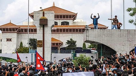 इस तस्वीर में एक घर के सामने काफी लोगों की भीड़ दिखाई दे रही है, और भीड़ के सामने एक सुंदर सा घर है। घर की छत पर दो-तीन लोग खड़े हैं।