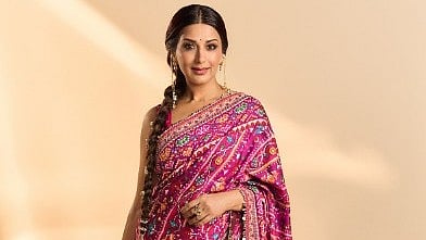 सोनाली बेंद्रे गुलाबी साड़ी पहने खड़ी है 
