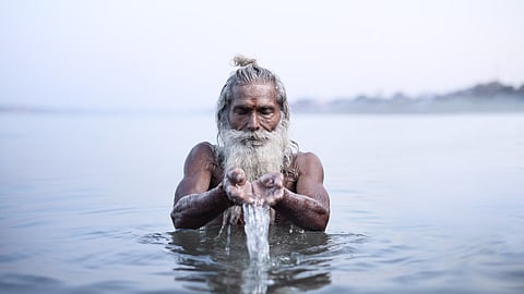 एक व्यक्ति नदी जल में अर्पित करते हुए नजर आ रहा है।