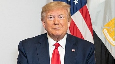 अमेरिकी राष्ट्रपति डोनाल्ड ट्रंप सफ़ेद शर्ट और ब्लैक कोर्ट पहने बैठे है 