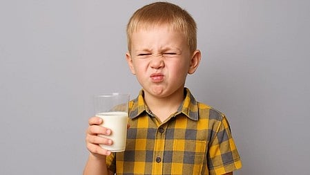 एक बच्चा हाथ में दूध लिए खड़ा है और उनसे पीले रंग का शर्ट पहना है 