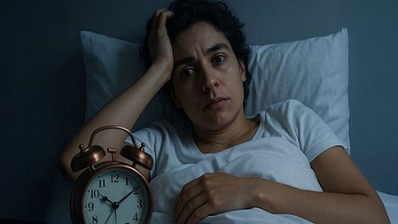 एक महिला सफ़ीद कपड़ा पहने बेड पर लेटी है  माथे पर हाथ रख कर 