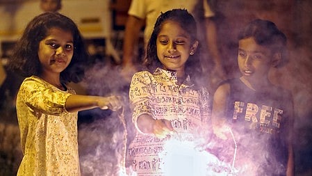 तीन बच्चियाँ छुरछुरी जला कर स्माइल करते हुए है 