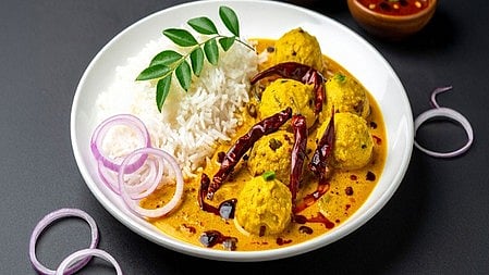  वाइट कलर की थाली में कढ़ी-चावल और थोड़ा सा प्याज रखा है  