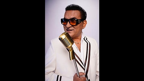 एक आदमी खड़ा होकर स्टैंडिंग माइक्रोफोन पकड़े हुए गा रहा है।
