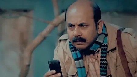 तस्वीर में खड़ा एक आदमी मुस्कुराते हुए कैमरे की ओर देखता हुआ।