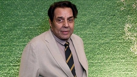 चित्र में अभिनेता धर्मेंद्र दिखाई दे रहे हैं, कैमरे की ओर शांत भाव से देखते हुए।