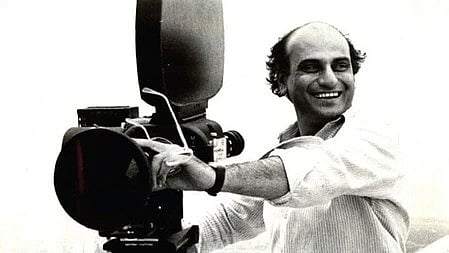 एक व्यक्ति सिनेमैटोग्राफी कैमरा लिए खड़ा|