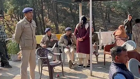 पुलिस अधिकारी खड़े और अन्य लोग बैठे नजर आ रहे हैं|