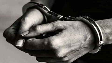 इस इमेज में हाथों को हथकड़ी में देखा का बोर्ड देखा जा सकता है। 