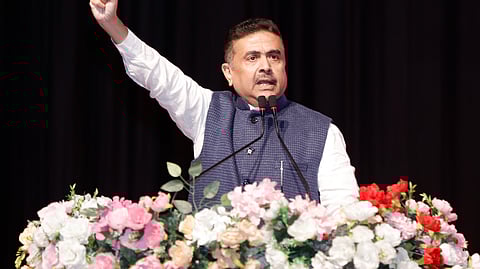 एक व्यक्ति मंच पर भाषण देते हुए दिखाई दे रहा है, सामने फूलों से सजा पोडियम है और वह हाथ उठाकर इशारा कर रहा है।