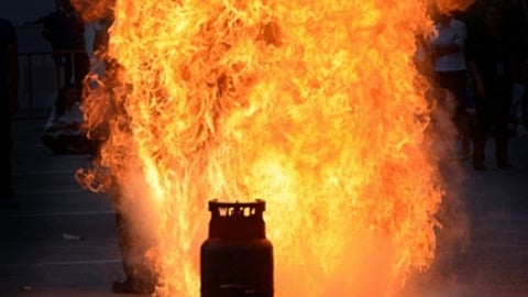 सड़क पर रखा एक गैस सिलेंडर आग की लपटों में घिरा हुआ है, सिलेंडर से ऊँची लपटें उठती दिखाई दे रही हैं।
