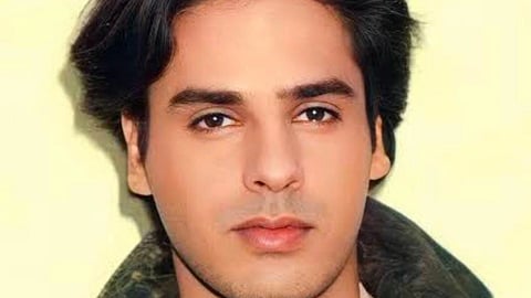 हल्के पीले बैकग्राउंड के सामने अभिनेता राहुल रॉय का क्लोज़-अप पोर्ट्रेट लुक। उन्होंने गहरे रंग का जैकेट या स्वेटर पहना हुआ है।
