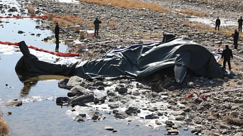 नदी किनारे हेलीकॉप्टर दुर्घटना का मलबा पड़ा है, आसपास जांच करती सुरक्षा एजेंसियों की टीम दिखाई दे रही है।