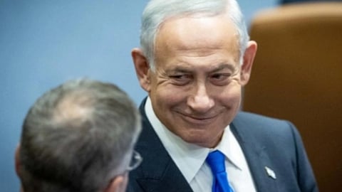 इजरायल के प्रधानमंत्री एक सरकारी बैठक के दौरान सूट-टाई पहने मुस्कुराते हुए किसी अधिकारी से बातचीत करते हुए नजर आ रहे हैं।