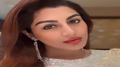 क्लोज़-अप तस्वीर में एक महिला हल्के मेकअप, गहरे रंग की लिपस्टिक और लंबे झुमके पहने कैमरे की ओर देखती हुई नजर आ रही हैं।