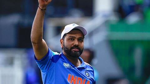 भारतीय क्रिकेटर रोहित शर्मा नीली टीम इंडिया जर्सी और सफेद कैप पहने मैदान पर हाथ उठाकर अभिवादन करते हुए दिखाई दे रहे हैं।