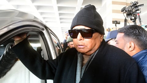 काला चश्मा लगाए और गाड़ी को हाथ से पकड़े हुए लालू यादव, कंधे पर शॉल ओढ़ रखी है। 
