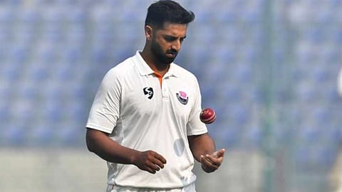 सफ़ेद जर्सी में एक गेंदबाज नज़र आ रहा है, जिसके हाथ में लाल रंग की गेंद है। 