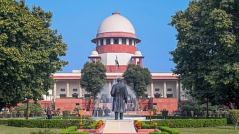 सुप्रीम कोर्ट के आस पास पेड़ पौधे नज़र आ रहे हैं और सामने मूर्ति नज़र आ रही है। 
