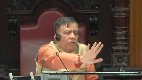 विधानसभा में बैठे हुए स्पीकर जो हाथ से रोकने का इशारा कर रहे हैं और उन्होंने भगवा कुर्ता पहन रखा है  
