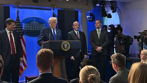 व्हाइट हाउस के प्रेस ब्रीफिंग कक्ष में अमेरिकी राष्ट्रपति डोनाल्ड ट्रंप पोडियम पर संबोधित करते हुए नजर आ रहे हैं, उनके साथ अधिकारी खड़े हैं और सामने पत्रकार व कैमरे मौजूद हैं।
