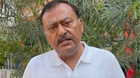 सफ़ेद टी शर्ट में कैमरे पर बोलते भारतीय नेता और पीछे पौधे दिखाई दे रहे हैं। 