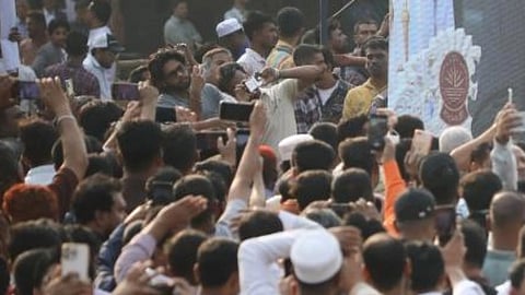 भीड़भाड़ वाली सड़क पर बड़ी भीड़, कई लोग मोबाइल से वीडियो बनाते हुए और अफरा-तफरी का माहौल।