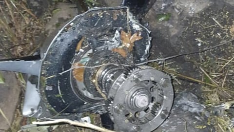 जंगल में दुर्घटनाग्रस्त एयर एम्बुलेंस के मलबे का क्लोज़-अप शॉट, जिसमें टूटा हुआ इंजन और धातु के क्षतिग्रस्त हिस्से जमीन पर बिखरे दिखाई दे रहे हैं।
